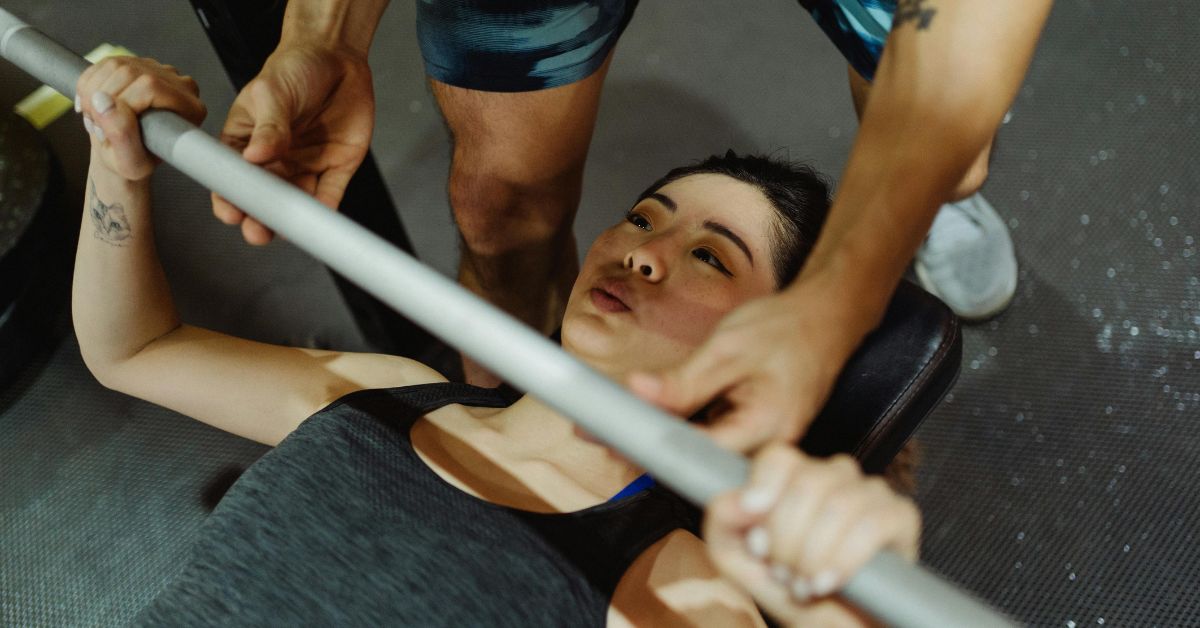 Woman performing bench press exercise with guidance in a gym setting.