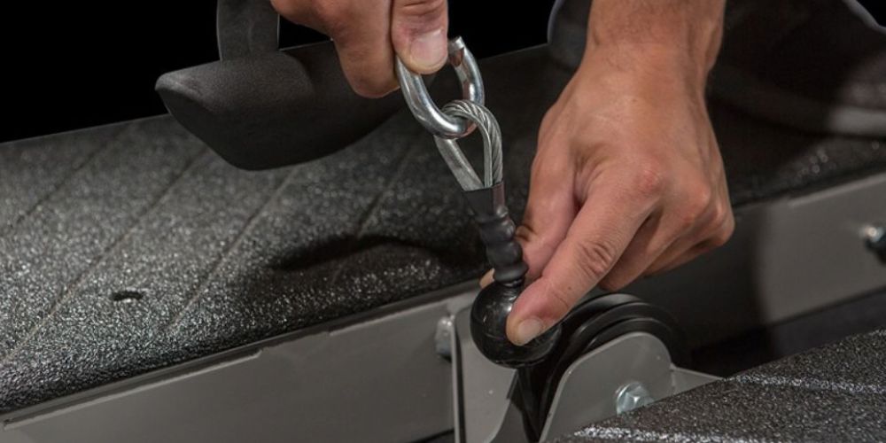 Hands attaching a cable to a fitness machine clip.
